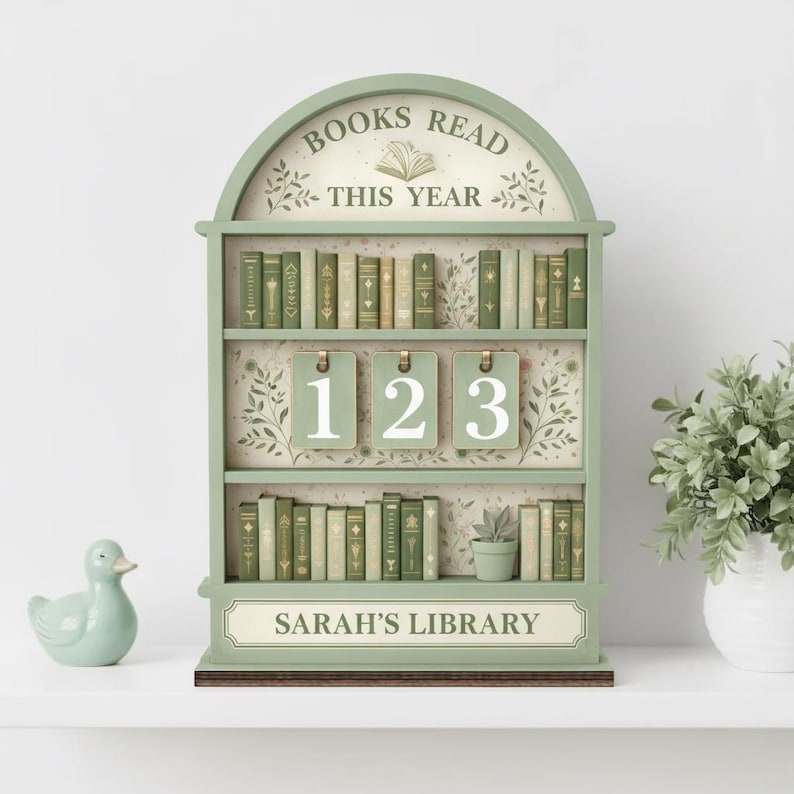 Puede incluir: Un estante en forma de librer&iacute;a verde salvia con el texto "BOOKS READ THIS YEAR" y "SARAH'S LIBRARY". Los estantes est&aacute;n llenos de libros en miniatura. El rastreador tiene tres etiquetas numeradas: 1, 2 y 3.