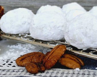 May include: A close-up of a white, powdered cookie on a wire rack. The cookies are surrounded by pecan halves.