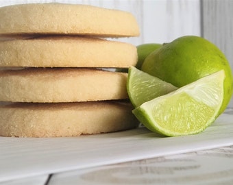 May include: A stack of four light brown shortbread cookies next to lime slices and whole limes.