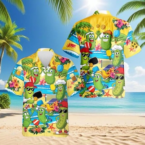 May include: Yellow Hawaiian shirt featuring cartoon pickles playing pickleball on a beach. The shirt has a button-down front and short sleeves. The design includes palm trees, flowers, and a beach scene. The shirt is a fun and playful design.