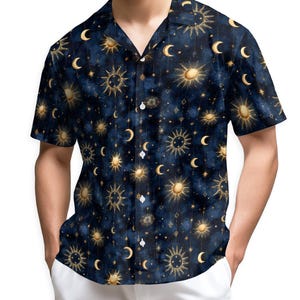 Puede incluir: Camisa azul oscuro de manga corta con un patrón celestial de soles, lunas y estrellas doradas. La camisa tiene cuello de campamento y se combina con pantalones blancos. El diseño de la camisa presenta un efecto acuarela.