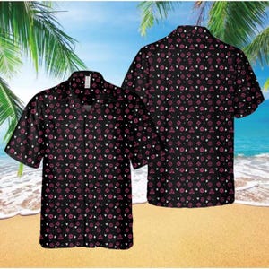 May include: Black short-sleeved shirt featuring a repeating pattern of pink and white geometric shapes. The shirt is displayed on a beach with palm trees and a blue sky in the background. The shirt is a casual style.