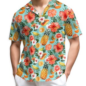 Può includere: Una camicia a maniche corte con un motivo di frutta tropicale e fiori. La camicia presenta uno sfondo azzurro con illustrazioni di ananas, fiori di ibisco, papaya, arance e banane. Un capo vibrante e colorato.