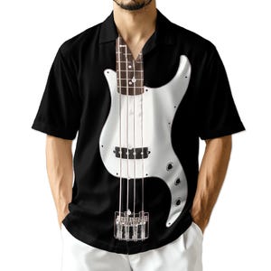 May include: Black short-sleeved shirt featuring a silver bass guitar design. The bass guitar graphic is centered on the shirt, with the neck of the guitar extending up towards the collar. The shirt has a classic button-down collar.