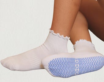 May include: A pair of white ankle socks featuring a ribbed texture and a ruffled lettuce-edge cuff. The soles of the socks are white with a light blue wavy grip pattern and the word ROUNDED printed in light blue on the bottom of the foot.