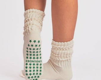 May include: Off-white slouchy crew socks featuring a textured, ribbed knit pattern on the upper section. The sole of the sock displays a pattern of small green stars and the word GROUNDED printed in green lettering across the bottom.