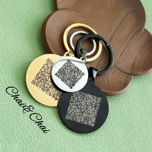 May include: Three circular keyrings in gold, silver, and black, each featuring a QR code pattern. The keyrings are attached to gold, silver, and black keyrings. The text "Chai & Chai" is visible in the lower left corner.
