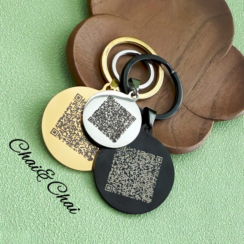 May include: Three circular keyrings in gold, silver, and black, each featuring a QR code pattern. The keyrings are attached to gold, silver, and black keyrings. The text "Chai & Chai" is visible in the lower left corner.