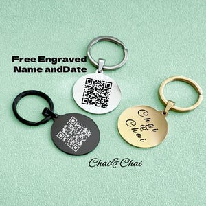 May include: Three round keyrings with different coloured metal rings. One is silver, one is black, and one is gold. The silver and black keyrings have a QR code engraved on them. The gold keyring has the words "Chai & Chai" engraved on it.