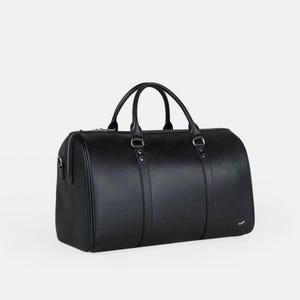 Pu&ograve; includere: Una borsa da viaggio nera di forma cilindrica. La borsa ha due manici e una chiusura a cerniera. La borsa &egrave; realizzata in un materiale liscio e ha finiture color argento. La borsa &egrave; lunga circa 50 cm.