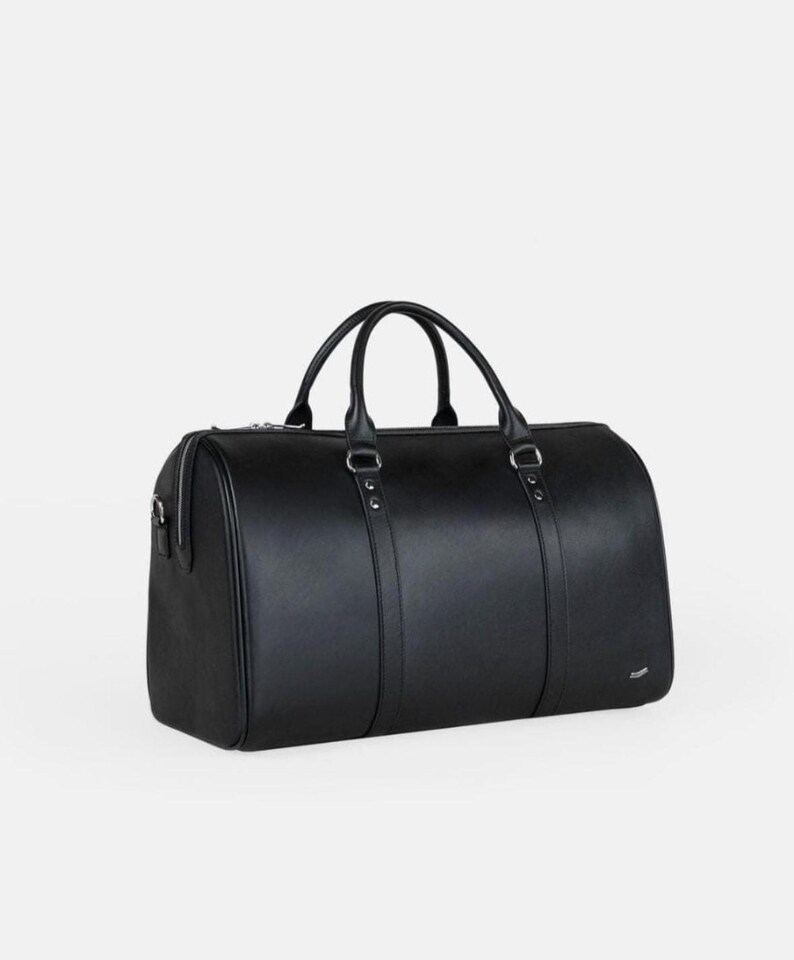 Pu&ograve; includere: Una borsa da viaggio nera di forma cilindrica. La borsa ha due manici e una chiusura a cerniera. La borsa &egrave; realizzata in un materiale liscio e ha finiture color argento. La borsa &egrave; lunga circa 50 cm.