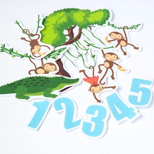 May include: A colorful jungle-themed illustration featuring a green crocodile, brown monkeys, a green tree, and blue numbers 1 through 5. The monkeys are hanging from vines. The image is on a white background.
