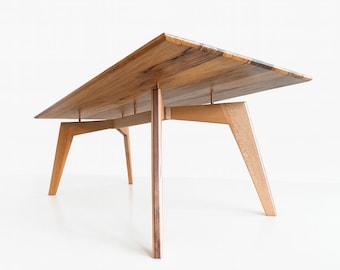 May include: A rectangular wooden table with a natural finish. The tabletop is supported by four angled legs and two central vertical supports. The table is approximately 60 inches long and 30 inches wide.