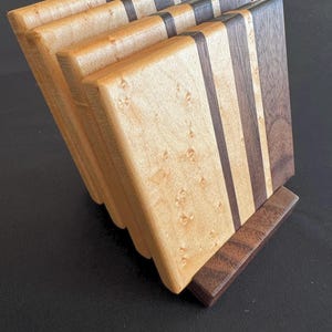 Könnte beinhalten: Ein Set aus vier Holzuntersetzern in einem Halter. Die Untersetzer sind aus hellem Holz mit dunklen Holzakzenten gefertigt. Der Halter ist aus dunklem Holz gefertigt. Die Untersetzer sind fächerförmig angeordnet.