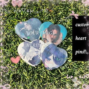 May include: Four heart-shaped pins with different images, including a person and anime-style characters. The pins are on a bed of green grass. Text on the pins reads "YOUR IMAGE HERE!" and "custom heart pins!!" in a black box.