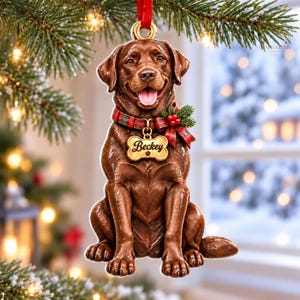 May include: A chocolate Labrador retriever Christmas ornament featuring a dog with a red and green plaid collar, a festive bow, and a gold bone-shaped tag with the name Beckey engraved on it, hanging from a red ribbon.