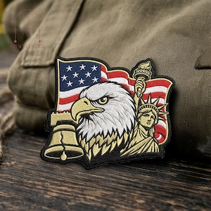 May include: Embroidered patch featuring an American flag, a bald eagle, the Liberty Bell, and the Statue of Liberty. The patch has a black border and is in shades of red, white, blue, and gold.