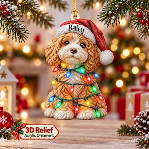 May include: A hanging ornament featuring a curly-haired brown and white puppy wearing a red Santa hat with the name Bailey printed on the white trim. The puppy is wrapped in a string of colourful glowing Christmas lights in red, blue, green, and yellow.
