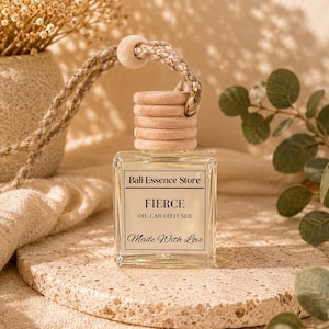 May include: A clear glass oil car diffuser bottle with a light wood cap and a braided hanging cord. The white label features the text Bali Essence Store, FIERCE, OIL CAR DIFFUSER, and Made With Love in black serif and script fonts.