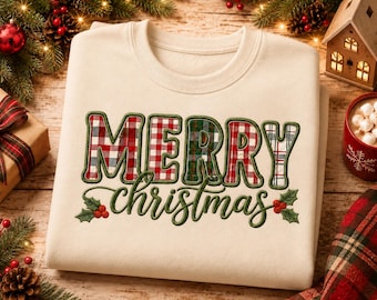 May include: A cream-colored crewneck sweatshirt featuring the text MERRY CHRISTMAS in a bold, embroidered style. The letters are filled with various red, green, and white plaid patterns, and the word christmas is accented with holly leaves and berries.