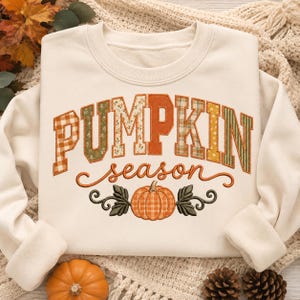 May include: A cream-coloured crewneck sweatshirt featuring the word PUMPKIN in large, multi-patterned block letters with plaid, floral, and solid orange fabrics. Below, the word season is written in cursive, followed by a plaid pumpkin graphic.