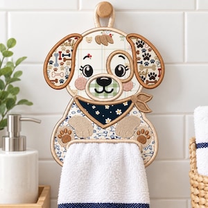 May include: A hanging kitchen towel holder shaped like a cartoon dog with a cream-colored face, brown ears, and a dark blue bandana with white flowers. The dog features embroidered paw prints, bones, and a white terry cloth towel hanging from its paws.