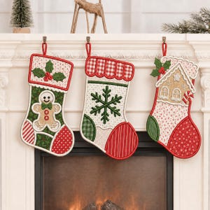 May include: Three Christmas stockings hanging in a row. The left stocking features a gingerbread man and holly. The center stocking displays a large green snowflake. The right stocking shows a gingerbread house with a candy cane and holly.