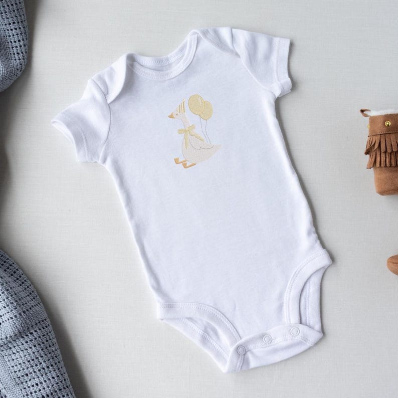 May include: White baby onesie with a whimsical goose graphic holding yellow balloons. The goose has a yellow bow and is wearing a party hat. The onesie has short sleeves and snap closures.