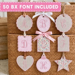 May include: A collection of nine fabric ornaments featuring embroidered letters A through I. The shapes include scalloped circles, squares, a heart, a rectangle, and a star, decorated with pink gingham, floral patterns, and solid beige fabric with pink trim.