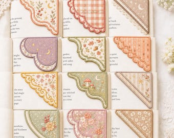 May include: A collection of twelve embroidered fabric corner bookmarks featuring various designs including floral patterns, plaid, mushrooms, moons, and stars. Each bookmark has a distinct shape with scalloped or straight edges.