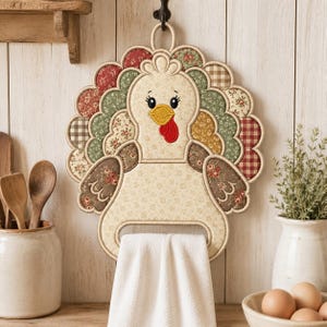 Peut inclure: Un porte-serviette de cuisine en tissu en forme de dinde avec un corps crème à motif floral, un bec jaune et une caroncule rouge. La dinde possède une queue festonnée composée de divers empiècements en tissu à motifs dans les tons rouge, vert et marron.