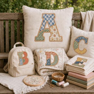 Könnte beinhalten: Eine Sammlung cremefarbener Textilartikel, bestehend aus einem großen quadratischen Kissen mit einem Buchstaben A, einem kleinen Rucksack mit einem Buchstaben B, einem quadratischen Kissen mit einem Buchstaben C, einer gefalteten Steppdecke mit einem Buchstaben D und einem gefalteten Handtuch mit einem Buchstaben E.