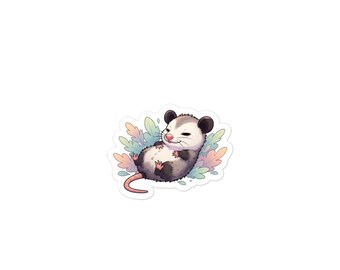 Könnte beinhalten: Ein Aufkleber mit einem Cartoon-Opossum, das entspannt auf dem Rücken liegt. Das Opossum hat graues Fell, schwarze Ohren und einen rosa Schwanz. Es liegt auf einem Bett aus pastellfarbenen Blättern. Der Aufkleber hat einen weißen Rand.