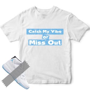 May include: White t-shirt with the text "Catch My Vibe or Miss Out" in light blue. A pair of white and light blue sneakers is partially visible in the lower left corner.