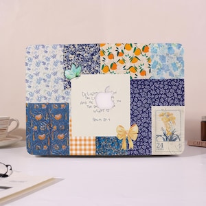 Op de afbeelding: Een laptophoes met een patchwork ontwerp van bloemen-, oranje- en ruitpatronen. Een vlinder en een strik sieren de hoes. Een handgeschreven notitie met de tekst "Delight the Lord and He the desires of your heart" is gecentreerd.