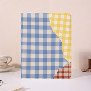 Puede incluir: Una funda rectangular para tableta con un diseño en capas que presenta un gran patrón de cuadros vichy azules y blancos, una sección de cuadros amarillos y blancos arriba a la derecha y un pequeño acento de cuadros rojos y blancos abajo.
