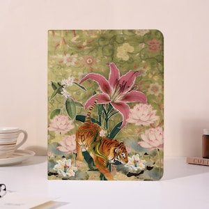 Op de afbeelding: Een decoratieve tablethoes met een tijgerillustratie te midden van roze lelies en lotusbloemen. De achtergrond is een groen bloemenpatroon. De tijger is oranje met zwarte strepen en groene accenten.