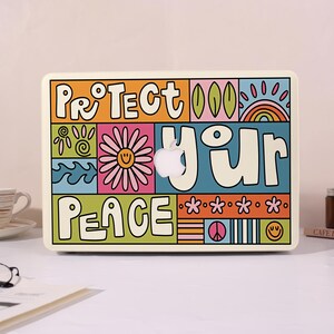 May include: A laptop skin featuring a colourful graphic design with the text "PROTECT YOUR PEACE". The artwork includes a daisy, a rainbow, waves, and smiley faces in shades of orange, pink, blue, and green, with a central cutout for an Apple logo.