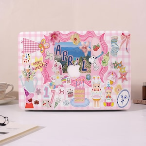 Könnte beinhalten: Eine Laptop-Hülle mit rosa-weißem Karomuster, verziert mit bunten Aufklebern. Die Aufkleber zeigen Blumen, ein Einhorn, Snoopy, einen Kuchen und das Wort "April". Es gibt auch eine "Happy Birthday"-Nachricht.