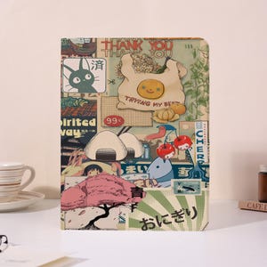 Può includere: Un taccuino colorato con un collage di illustrazioni di ispirazione giapponese. La copertina presenta un gatto, cibo e il testo "THANK YOU" e "TRYING MY BEST". Il design include un albero di ciliegio rosa e altri elementi grafici.