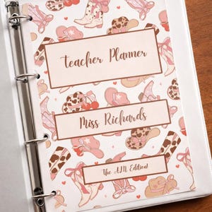 K&ouml;nnte beinhalten: Ein wei&szlig;er Ordner mit einem Lehrerplaner-Cover mit einem sich wiederholenden Muster aus rosa Cowboy-Stiefeln, H&uuml;ten und Schleifen. Das Cover enth&auml;lt den Text "Teacher Planner", "Miss Richards" und "The AM Edition!"
