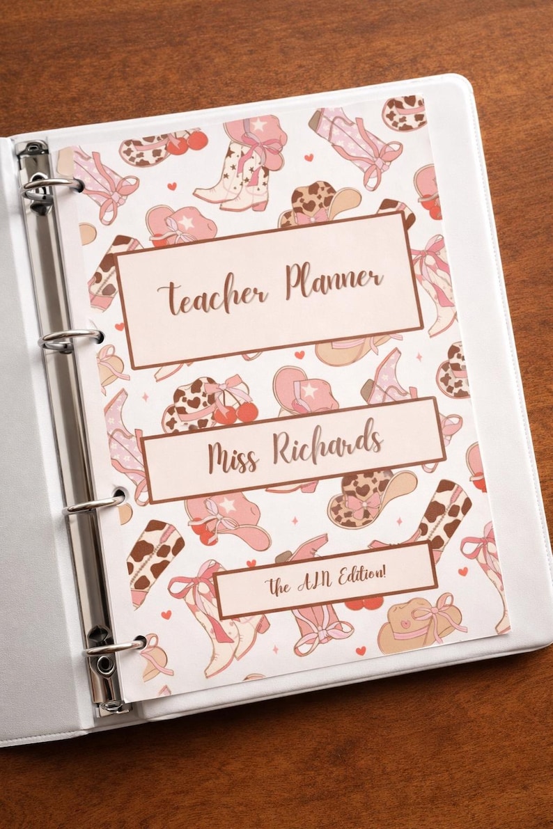 K&ouml;nnte beinhalten: Ein wei&szlig;er Ordner mit einem Lehrerplaner-Cover mit einem sich wiederholenden Muster aus rosa Cowboy-Stiefeln, H&uuml;ten und Schleifen. Das Cover enth&auml;lt den Text "Teacher Planner", "Miss Richards" und "The AM Edition!"