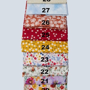 May include: A stack of fabric swatches in various floral and patterned designs. The colors include red, yellow, blue, and cream. Each swatch is labeled with a number from 20 to 28.
