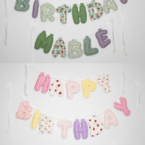 May include: Fabric banners with the words "HAPPY BIRTHDAY MABLE" and "HAPPY BIRTHDAY REMI" in various colors and patterns. The letters are made of soft fabric and strung on white ribbons, perfect for a birthday celebration.