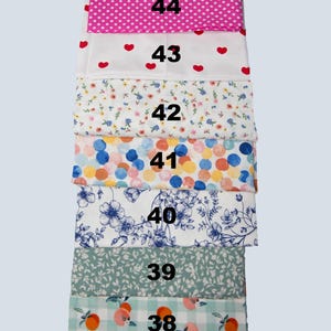 May include: A stack of patterned fabric samples. The fabrics include pink polka dots, red hearts, floral, colorful circles, blue floral, green leaves, and peach gingham. Each fabric is labeled with a number from 38 to 44.