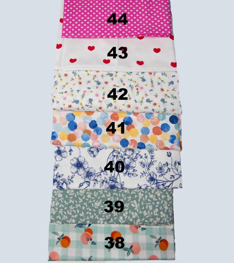 May include: A stack of patterned fabric samples. The fabrics include pink polka dots, red hearts, floral, colorful circles, blue floral, green leaves, and peach gingham. Each fabric is labeled with a number from 38 to 44.