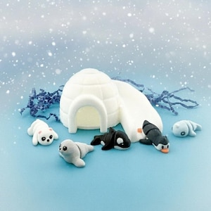 May include: A whimsical scene featuring a white igloo and several small animal figurines, including seals, penguins, and a killer whale, set against a snowy blue backdrop. The figurines are detailed and colorful, creating a playful winter theme.