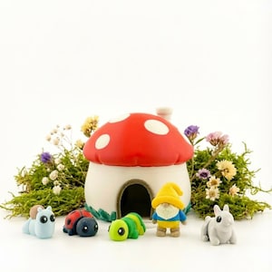 May include: A miniature fairy garden scene with a red and white mushroom house, and small figurines of a snail, ladybug, caterpillar, gnome, and bunny. The scene is decorated with green moss and colourful flowers.