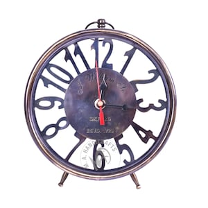 Op de afbeelding: Antieke messing klok met een skelet wijzerplaat. De klok heeft een donker messing afwerking, Romeinse cijfers en de tekst "J. William & Co. Oxford Estd. 1720". De klok heeft een rode secondewijzer en drie kleine pootjes.