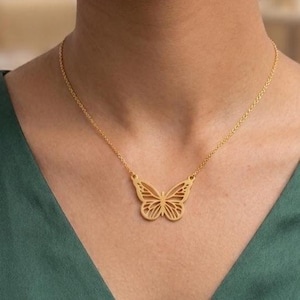 May include: A gold-toned necklace featuring a delicate, openwork butterfly pendant suspended from a fine chain. The butterfly design showcases intricate, symmetrical cut-out details across its wings, creating a lightweight and airy appearance.